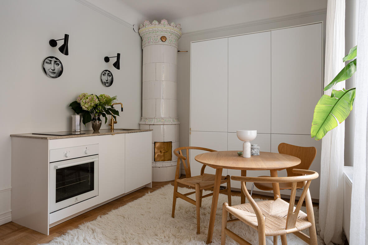 White kitchen and dining area with a tiled stove and sculptural Fornasetti wall plates.